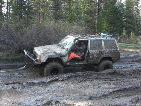 1995 Ford Bronco - A driver navigates a muddy trail in a heavily soiled Jeep Cherokee XJ.