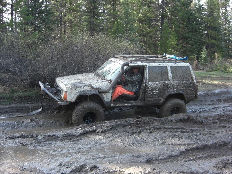 Mud-covered white Jeep Cherokee XJ stuck in mud with snorkel and aftermarket bumper