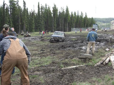 1995 Ford Bronco - An off-road vehicle is stuck in a muddy field during an event, with spectators nearby.