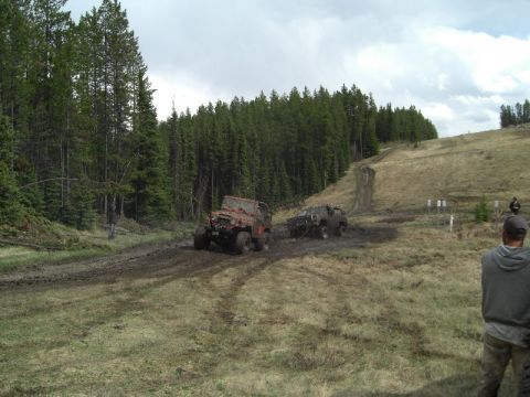 1995 Ford Bronco - Off-road vehicles navigate a muddy trail during an outdoor event.