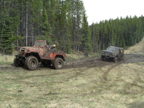 1995 Ford Bronco - Two off-road vehicles are stuck in the mud, with one attempting to tow the other out.