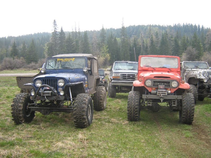 Red Toyota Land Cruiser FJ40 front view with blue Jeep and Ford truck behind