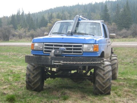 1995 Ford Bronco - Modified blue truck with oversized tires and snorkel, parked in a grassy field.