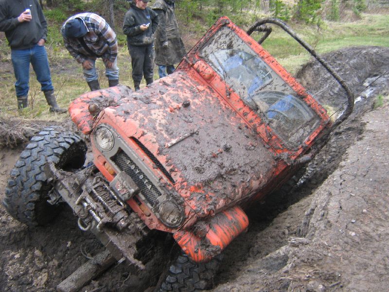 Orange Toyota Land Cruiser stuck in a muddy ditch with people watching