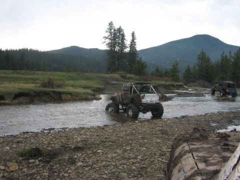 1995 Ford Bronco - Modified off-road vehicles navigate a rocky stream bed in a natural landscape.