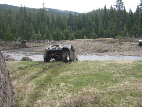 1995 Ford Bronco - A heavily modified off-road vehicle navigates a grassy bank next to a river, with another vehicle visible in the distance.