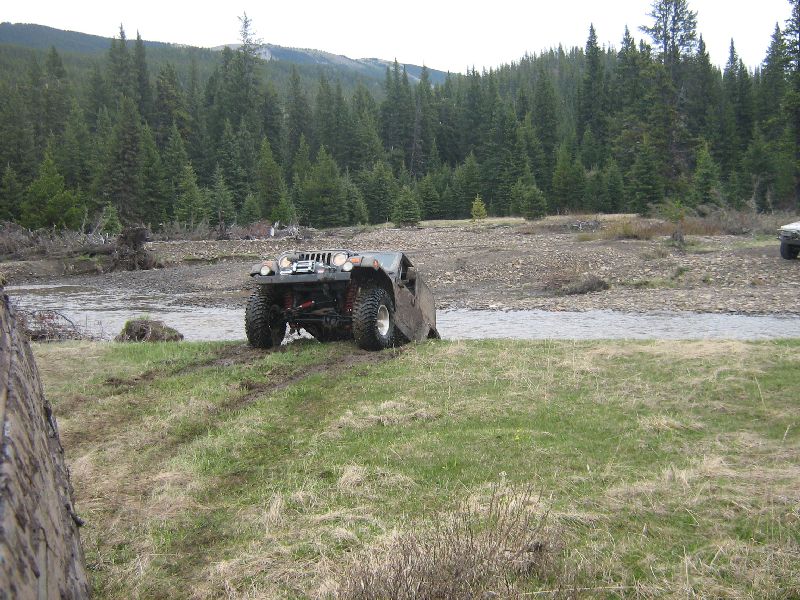 Modified off-road vehicle with large tires on grassy bank near river