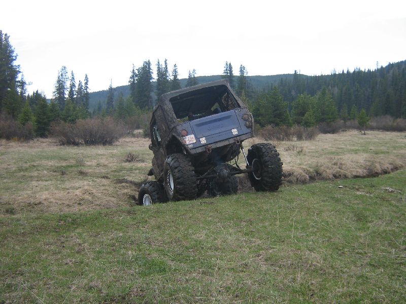 Blue off-road vehicle with large tires stuck in a grassy ditch, rear view