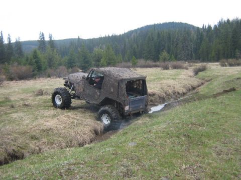 1995 Ford Bronco - A heavily modified Jeep Wrangler navigates a muddy creek bed during an off-road excursion.