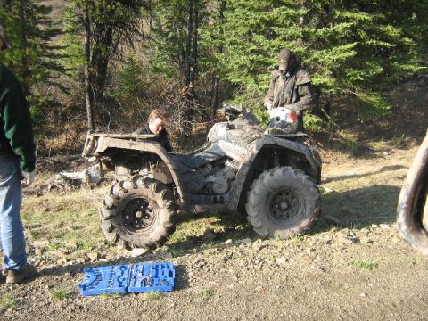 1995 Ford Bronco - An all-terrain vehicle sits on a dirt path, with two individuals nearby and a toolbox on the ground.