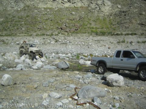 1987 Suzuki Samurai - Two off-road vehicles are stuck in a rocky riverbed, connected by a tow strap.