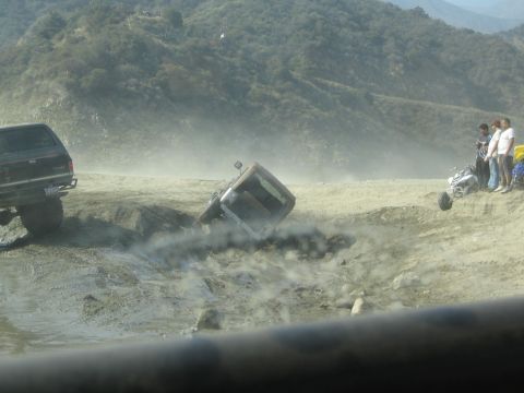 1987 Suzuki Samurai - Several off-road vehicles are stuck in a muddy ditch, with onlookers observing the scene.