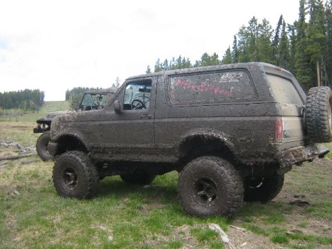 1995 Ford Bronco - This heavily mud-caked SUV is parked off-road with another vehicle nearby.