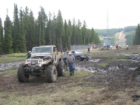 1995 Ford Bronco - Off-road vehicles navigate a muddy terrain with trees and a radio tower in the background.