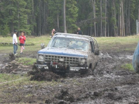 1995 Ford Bronco - This muddy scene captures a blue SUV, likely a 1973 Chevrolet K5 Blazer, deeply stuck in the mire during an off-road event.