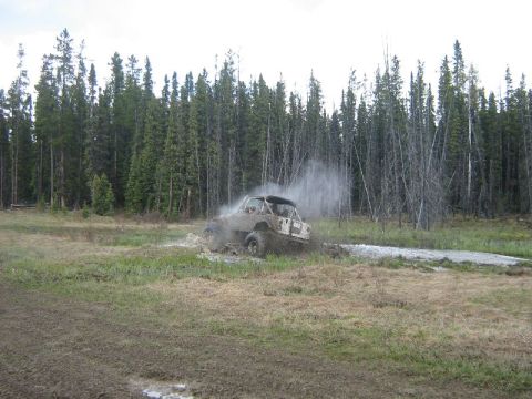 1995 Ford Bronco - An off-road vehicle navigates a muddy trail surrounded by dense forest.