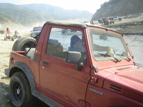 1987 Suzuki Samurai - Red 1987 Suzuki Samurai parked on a dirt path with other vehicles and ATVs nearby.