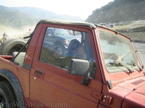 1987 Suzuki Samurai - A red 1987 Suzuki Samurai is parked on a dirt road with mountains in the distance, and people are visible inside.
