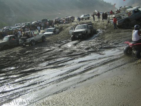 1987 Suzuki Samurai - Multiple off-road vehicles struggle through a deep mud pit under a hazy sky.