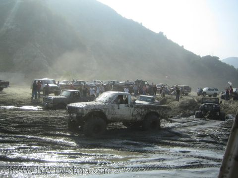 1987 Suzuki Samurai - Off-road vehicles stuck in mud with spectators watching.