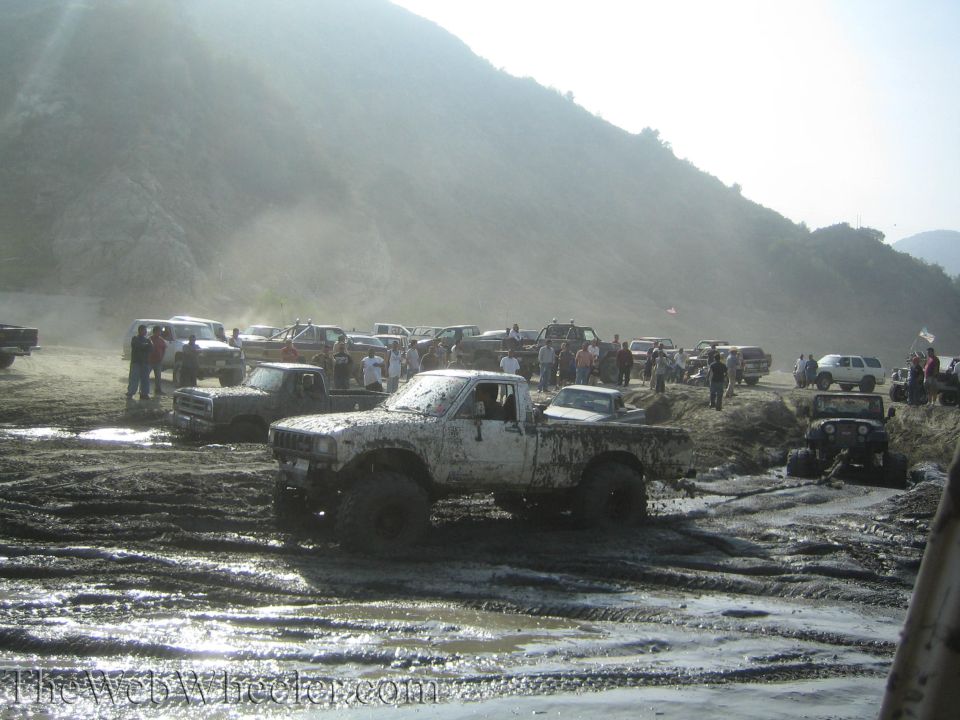 Muddy trucks and SUVs gathered in a muddy field with people around