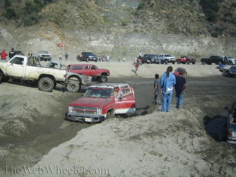 1987 Suzuki Samurai - Multiple off-road vehicles are seen in a muddy area with spectators.