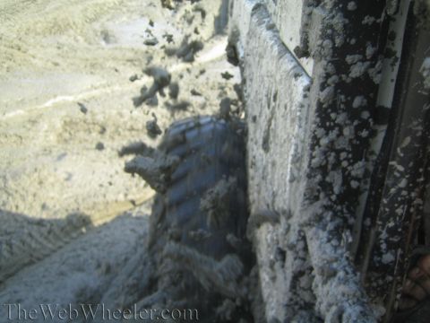 1987 Suzuki Samurai - A 1987 Suzuki Samurai's tire is stuck deep in mud, showing its off-road capabilities.
