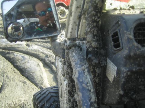 1987 Suzuki Samurai - A driver's reflection is seen in the side mirror of a mud-splattered 1987 Suzuki Samurai navigating a muddy terrain.