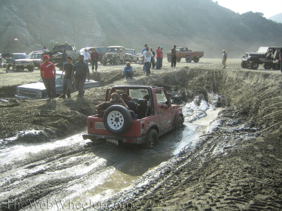Red 1987 Suzuki Samurai stuck in mud, rear view