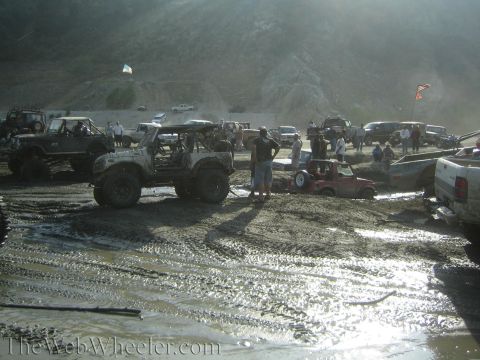 1987 Suzuki Samurai - A group of off-road vehicles are stuck in a muddy area, with several people observing the scene.