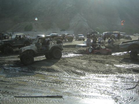 1987 Suzuki Samurai - Multiple off-road vehicles navigate a muddy terrain during an event.
