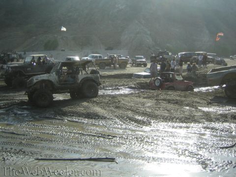 1987 Suzuki Samurai - Multiple off-road vehicles are stuck in a muddy terrain, with a hilly landscape in the background.