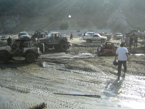 1987 Suzuki Samurai - A group of off-road vehicles navigate a challenging muddy terrain, with some vehicles partially submerged.