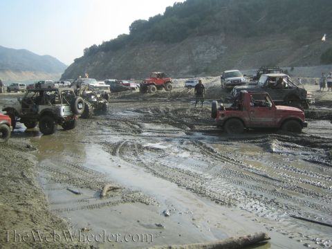 1987 Suzuki Samurai - Multiple off-road vehicles navigate a muddy terrain, with one red Suzuki Samurai prominently stuck.