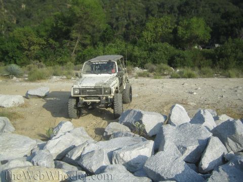 1987 Suzuki Samurai - A white 1987 Suzuki Samurai navigates a rocky terrain with trees in the background.