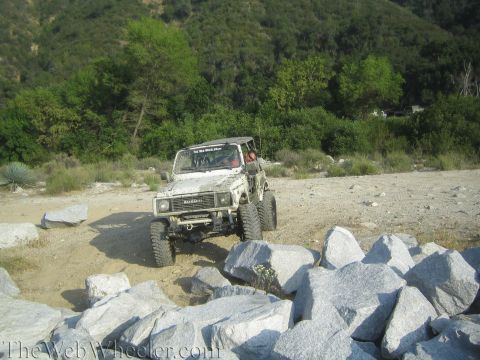 1987 Suzuki Samurai - A white 1987 Suzuki Samurai is shown off-roading through a rocky, natural landscape.