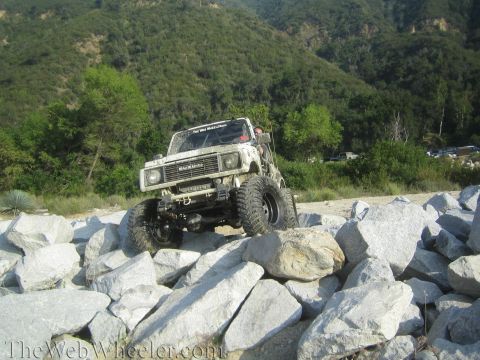 1987 Suzuki Samurai - A white 1987 Suzuki Samurai is shown off-roading over a rocky terrain.