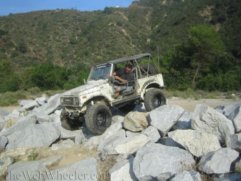 1987 Suzuki Samurai - A white 1987 Suzuki Samurai navigates a rocky terrain, demonstrating its off-road capabilities.