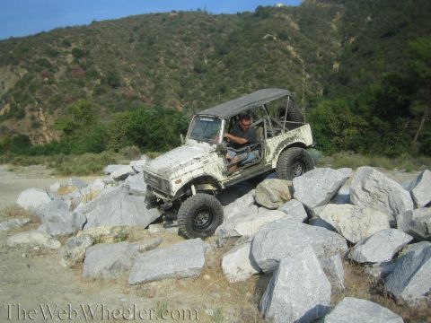 1987 Suzuki Samurai - A man drives a modified Suzuki Samurai over a rocky obstacle course on a sunny day.