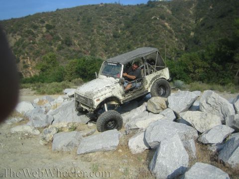 1987 Suzuki Samurai - A white 1987 Suzuki Samurai navigates a rocky terrain, demonstrating its off-road capabilities.