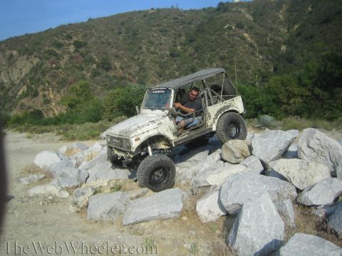 1987 Suzuki Samurai - A man drives a modified Suzuki Samurai over a rocky obstacle course in a dry, hilly area.