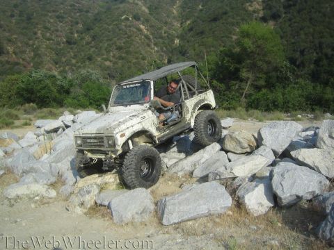 1987 Suzuki Samurai - A white Suzuki Samurai navigates a rocky terrain with a driver behind the wheel.