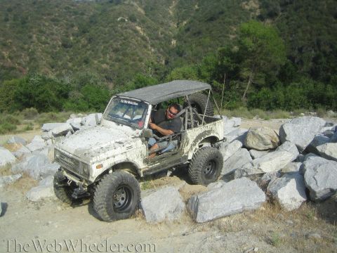 1987 Suzuki Samurai - This Suzuki Samurai is shown off-roading on a sunny day, surrounded by large rocks and hills.