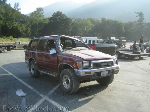 1987 Suzuki Samurai - A damaged red Toyota 4Runner sits in a parking lot with mountains in the background.