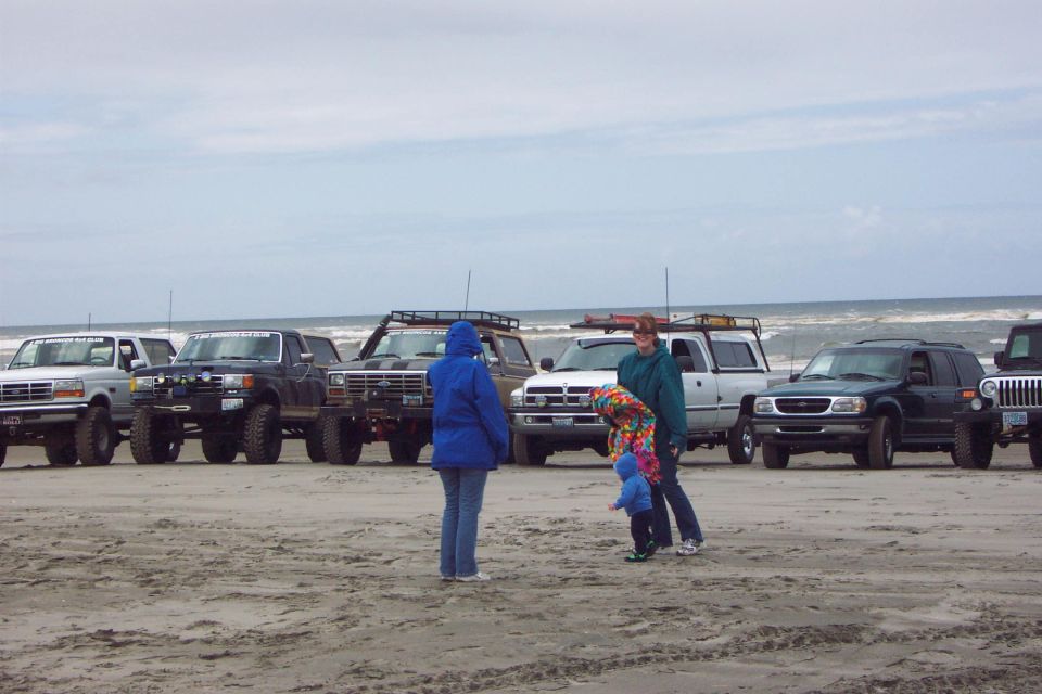 Lifted pickups and SUVs lined up on an overcast ocean beach with people