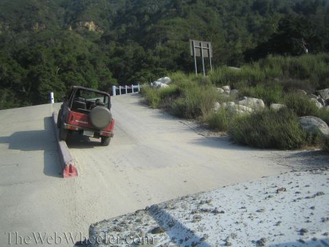 1987 Suzuki Samurai - A red Suzuki Samurai is parked on a dirt road, with a spare tire mounted on the rear. The vehicle is positioned on the side of the road, wi…