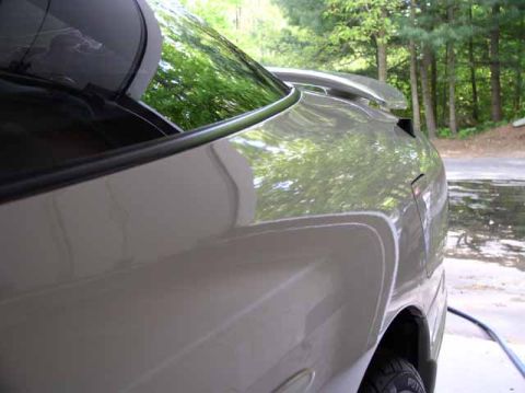 1996 Ford Probe - The rear quarter panel of a silver 1996 Ford Probe GT is visible, reflecting trees and sky.
