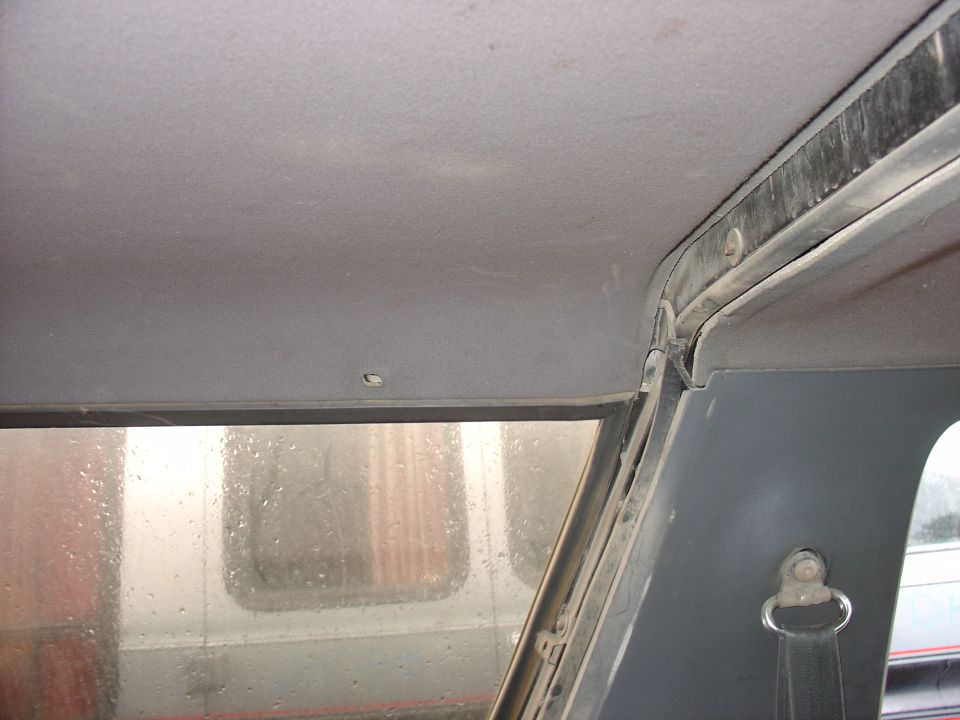 Gray headliner and window frame with visible water spots and dust. A seatbelt anchor is visible