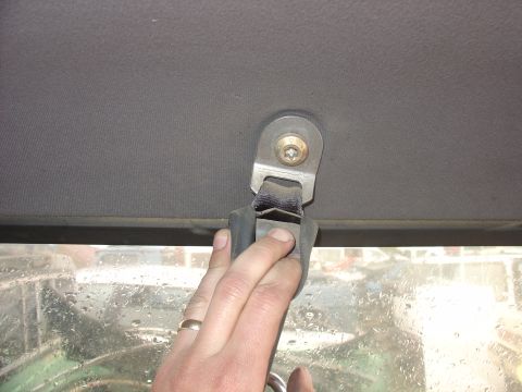 1988 Ford Bronco - Close-up of a seatbelt anchor point on the vehicle's headliner, with a hand visible adjusting the strap.