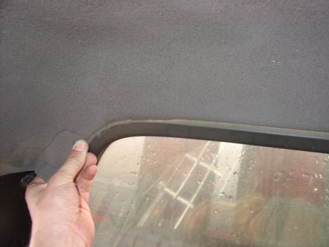 1988 Ford Bronco - Close-up of a car's interior headliner and window trim, with a hand pulling on the edge.